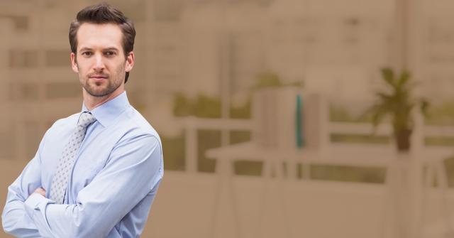 Young male businessman standing confidently with arms crossed in a modern office setting. Ideal for use in corporate materials, business communications, leadership promotions, and professional networking advertisements.