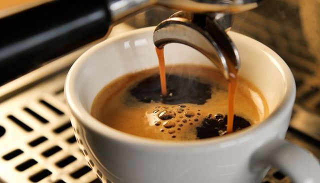 Pouring double espresso with rich crema from portafilter into white cup, barista machine closeup
