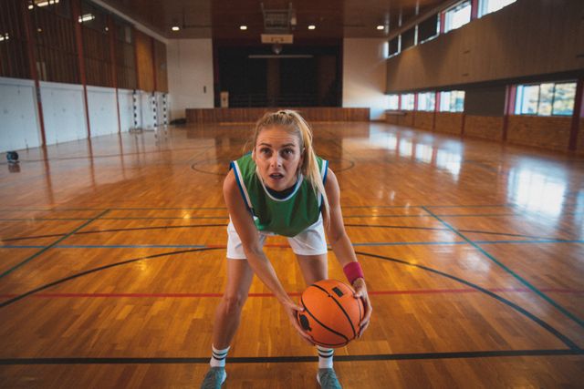 Caucasian female basketball player holding ball looking up at hoop in court. basketball sports team training at an indoor court.