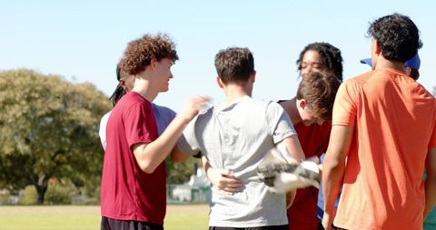 Diverse teen male teammates celebrating after cricket play on sunny outdoor field