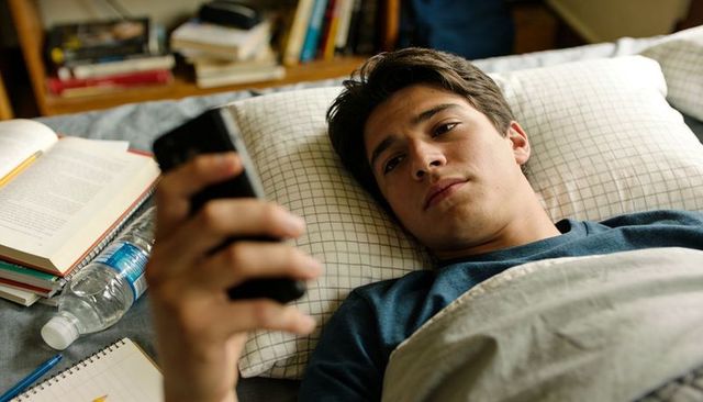 College student lying in bed holding smartphone late-night studying and digital distraction