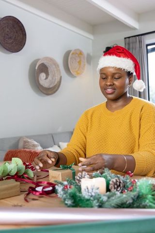 African american woman wearing santa hat wrapping holiday gifts at home cozy cheer