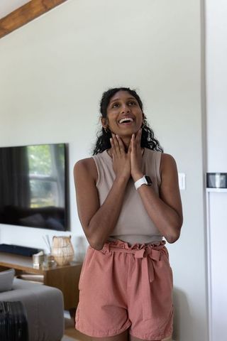 Young woman looking up and smiling at home wearing smartwatch and casual summer outfit