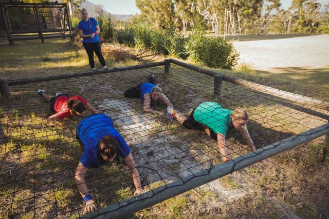 Group of fit women crawling under the net during obstacle course training in the boot camp