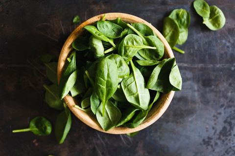 Fresh baby spinach leaves in wooden bowl showcasing vibrant green produce, rustic top view