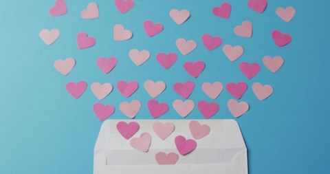 Open envelope emitting pink paper hearts on blue background
