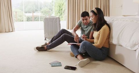 Young Couple Planning Trip with Notebook and Passports on Floor