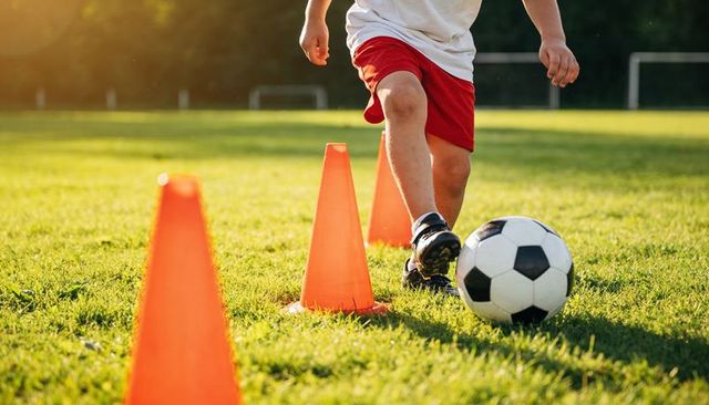 Youth soccer player dribbling ball through cone drill during sunny grass training session
