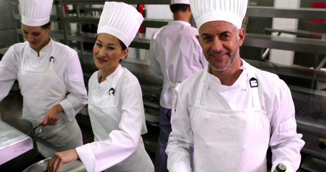 Professional chefs in white uniforms and hats engaging in food preparation in a modern, industrial kitchen. This image can be used for articles, brochures, or advertisements related to culinary arts, restaurant business, cooking classes, or professional chef training programs.