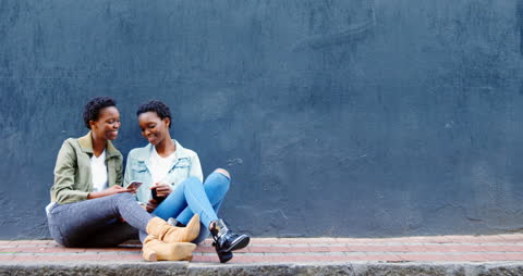 Twins Sitting on Sidewalk Engaging with Mobile Phone