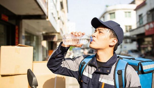 Urban delivery courier drinking water during shift with insulated backpack and parcels