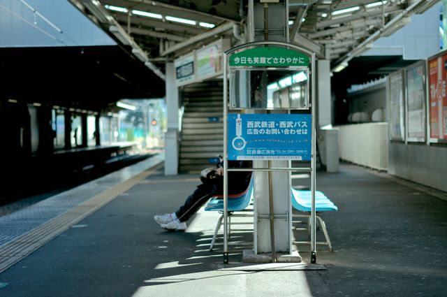 Photo depicts an almost empty train station with a single person sitting on a bench, suggesting themes of solitude and waiting. This type of image fits well for travel blogs, articles on urban life or public transportation systems, and marketing materials promoting solitary experiences or introspective moments in a busy city environment.