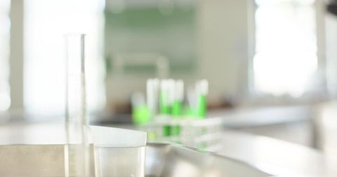 Laboratory glassware on stainless-steel bench with emerald test tubes and soft bokeh