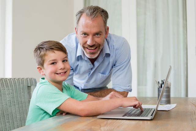 Portrait of smiling father and son using laptop at desk in study room