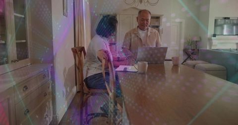 Adult son and mother working at wooden dining table with laptop, notebook and soft lights