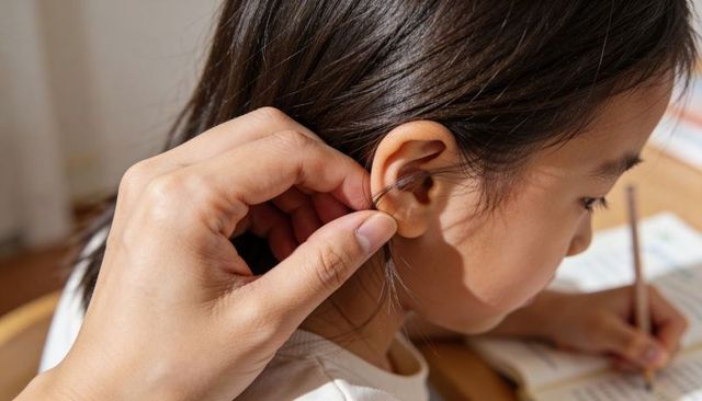 Tucking hair behind ear guiding child writing at sunlit desk caregiver helping home study