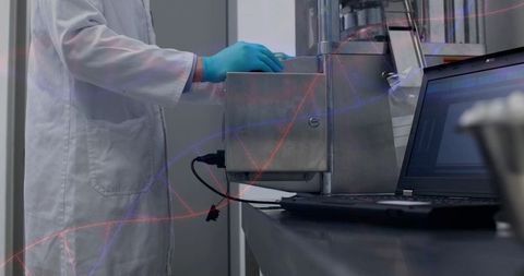 Lab technician adjusting stainless steel instrument beside laptop wearing teal gloves