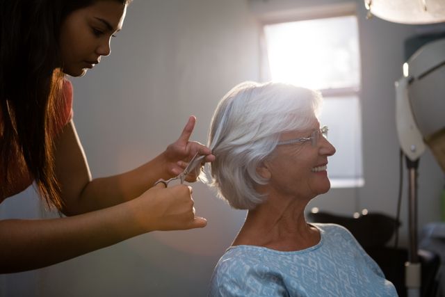 Senior woman receiving a haircut from a professional hair stylist in a salon. Ideal for use in articles or advertisements related to beauty services, senior care, personal grooming, and professional hairdressing. Can also be used in promotional materials for salons and hair care products.