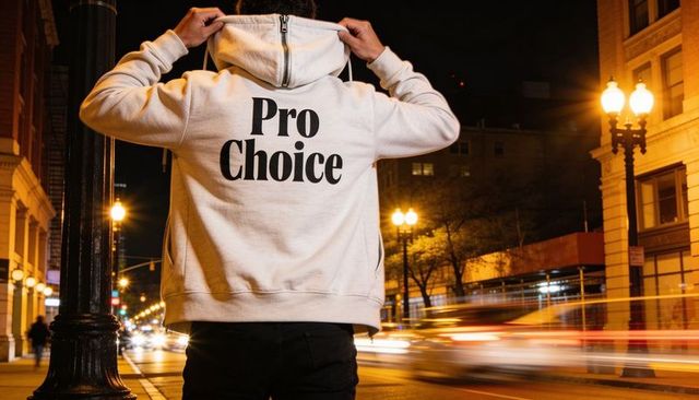 Man wearing pro choice hoodie adjusting hood on urban night street with light trails