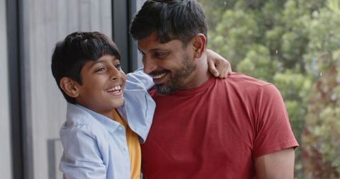 Father and Son Smiling Inside Modern Home by Large Window