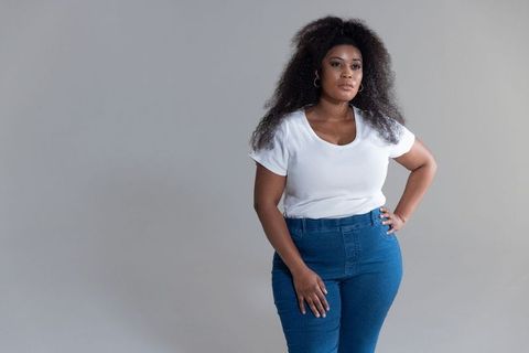 Confident african american woman posing in white tee and denim on neutral gray backdrop