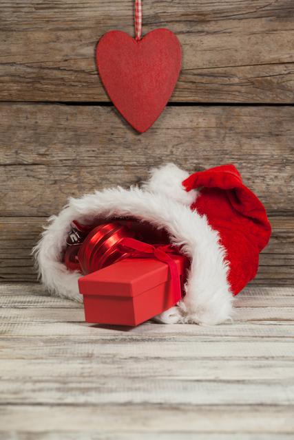 Christmas Bauble and Gift in Santa Hat on Wooden Background - Download Free Stock Photos Pikwizard.com