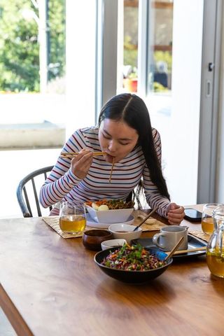 Woman enjoys asian noodles with chopsticks indoors