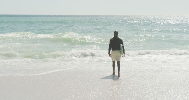 Man Standing on Beach Holding Surfboard Looking at Ocean - Download Free Stock Images Pikwizard.com