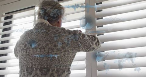 Senior woman adjusting window blinds with futuristic hud overlays, back view home
