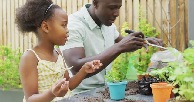 African American father and daughter planting seeds in garden, promoting outdoor activity, family bonding, and education about nature. Ideal for content on parent-child relationships, gardening tutorials, family activities, and educational experiences.