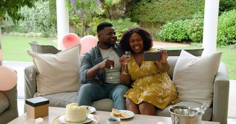 Happy Couple Celebrating with Cake and Smartphone on Outdoor Sofa