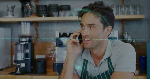 Barista talking on smartphone behind counter in cozy cafe with espresso machine