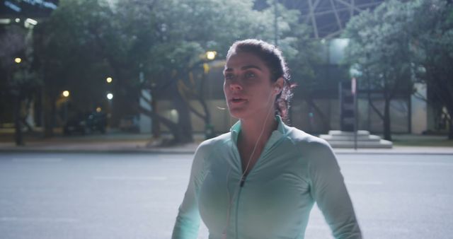 Young Caucasian woman jogging at night in an urban setting. She maintains her fitness routine with a late evening run through the city streets.