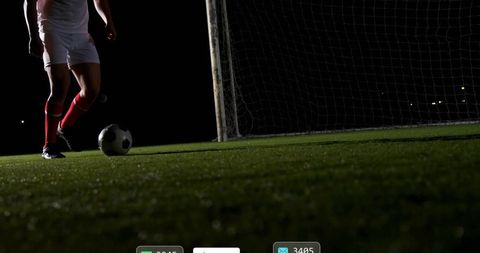 Night soccer player dribbling toward goal on floodlit turf low-angle dramatic action