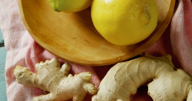 Top view of fresh ginger roots and lemons on wooden bowl and pink cloth. Ideal for health and wellness blogs, recipe websites, and natural remedy articles. Perfect for promoting organic food and healthy eating.