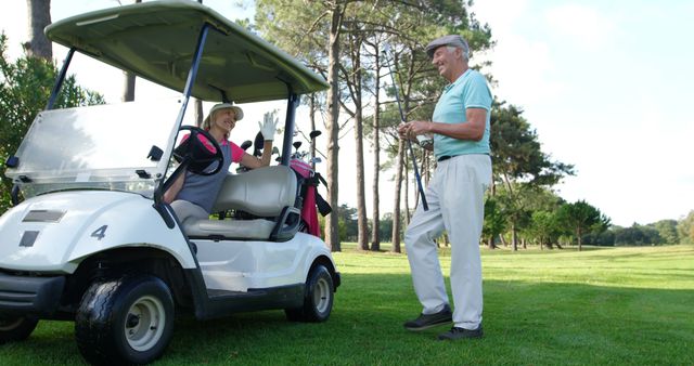 This image showcases a senior couple enjoying a day of golf. They are engaged in conversation near a golf cart, with the lush green course and trees providing a serene backdrop. Ideal for use in content related to healthy aging, outdoor sports, recreational activities, and senior lifestyle.