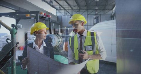 Engineers reviewing blueprint in hangar wearing yellow hardhats and hi-vis vests