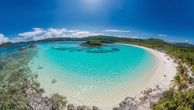 Turquoise crescent lagoon revealing coral patches and islet at tropical beach