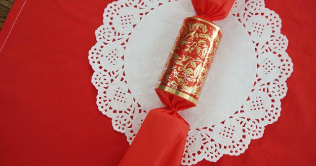 A red and gold Chinese firecracker decoration rests on a white paper doily against a vibrant red background, symbolizing celebration and festivity. Often used during Chinese New Year, these decorations represent warding off evil spirits and welcoming good luck and prosperity.