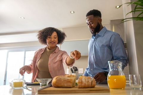 Couple Adding Seasoning to Fresh Bread in Modern Kitchen