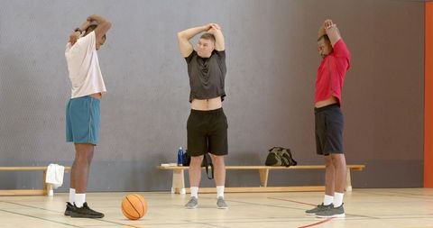 Three men stretching before basketball on indoor court, team warmup and athletic training