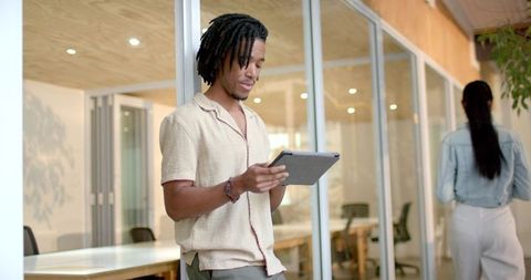 Young black professional using tablet in modern coworking corridor with glass offices