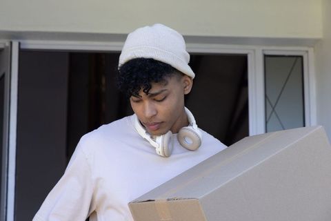 African american man carrying cardboard box at doorway wearing beanie and headphones