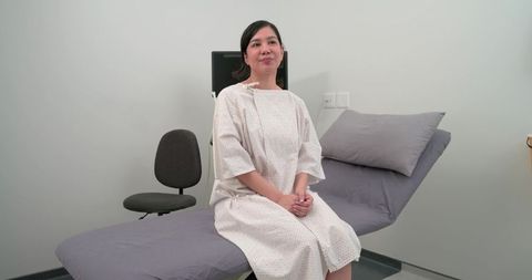Female patient sitting on exam table wearing medical gown in calm clinical environment
