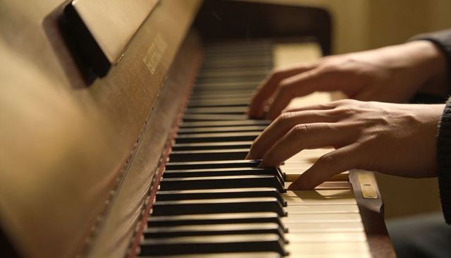 Playing upright piano keys: warm closeup of adult hands on wooden keyboard