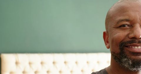 Smiling man relaxing on cream tufted sofa with green background