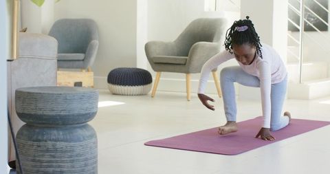 Young girl practicing yoga kneeling stretch on purple mat in modern living room