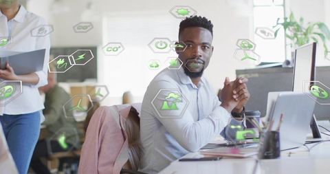 Manager collaborating on sustainability plan in open-plan office with green icons