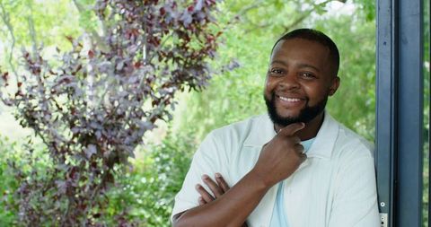 Smiling african man leaning on porch frame touching chin relaxed outdoor portrait