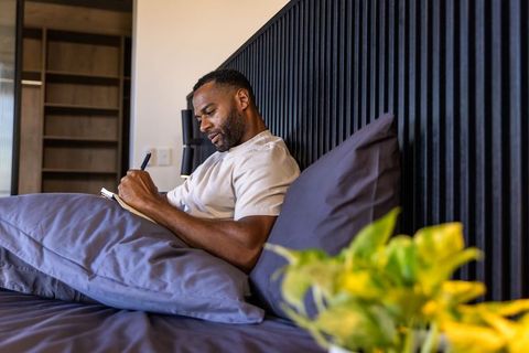 Mature african american man journaling in modern bedroom morning routine with notebook